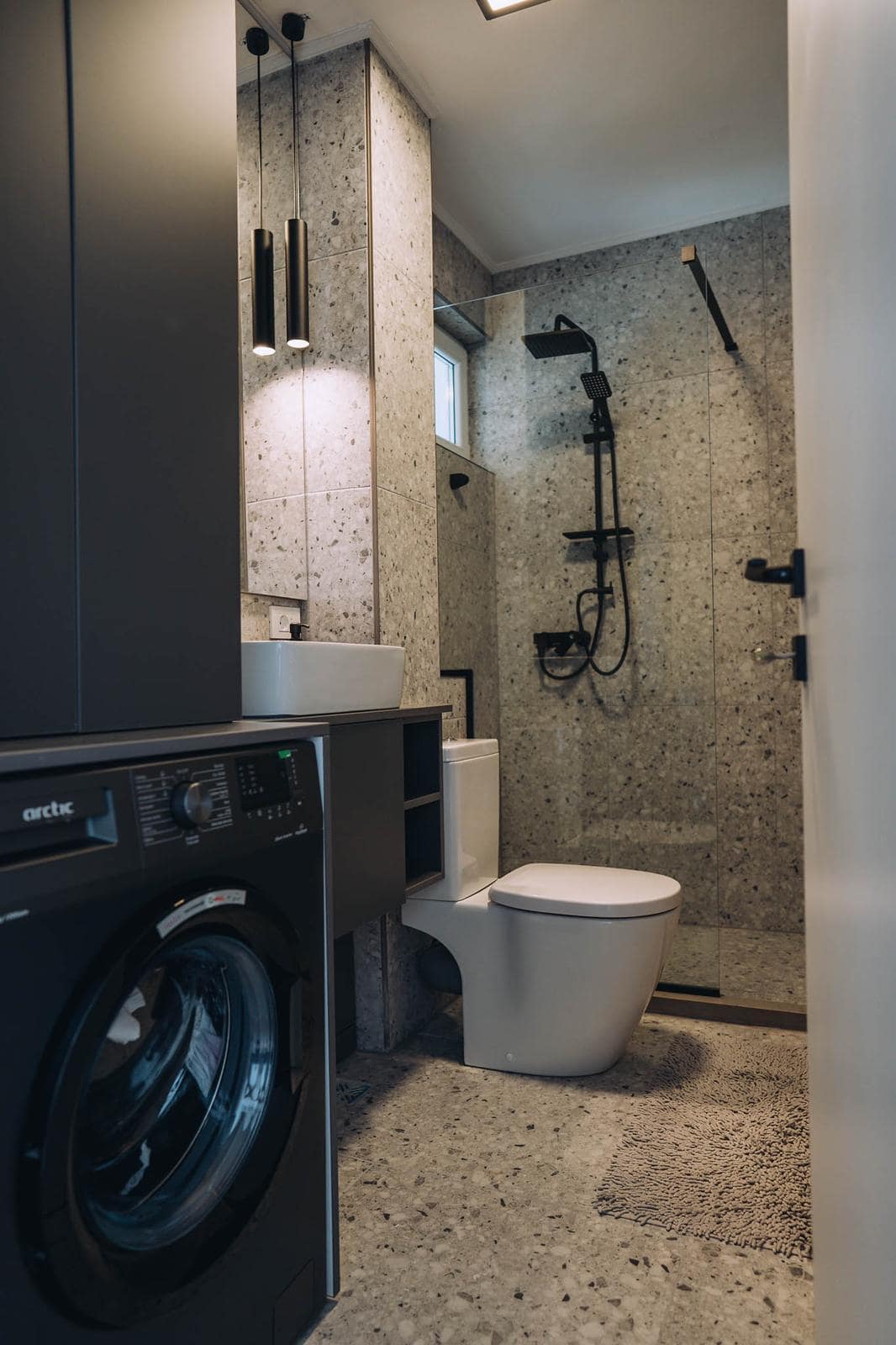 Compact terrazzo bathroom with a level-access shower and integrated washing machine