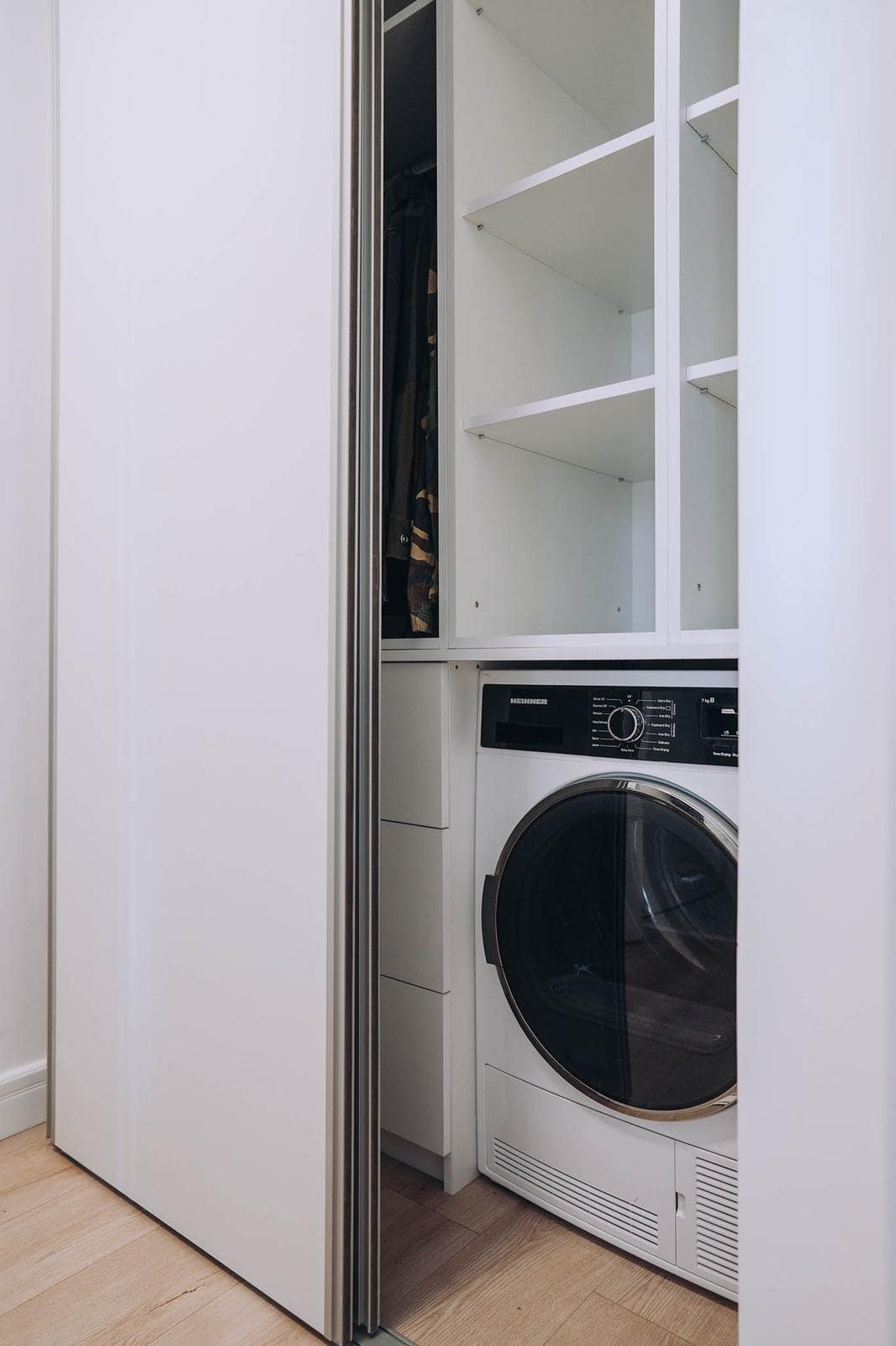 Utility zone concealed behind a sliding front, with shelving and a washing machine